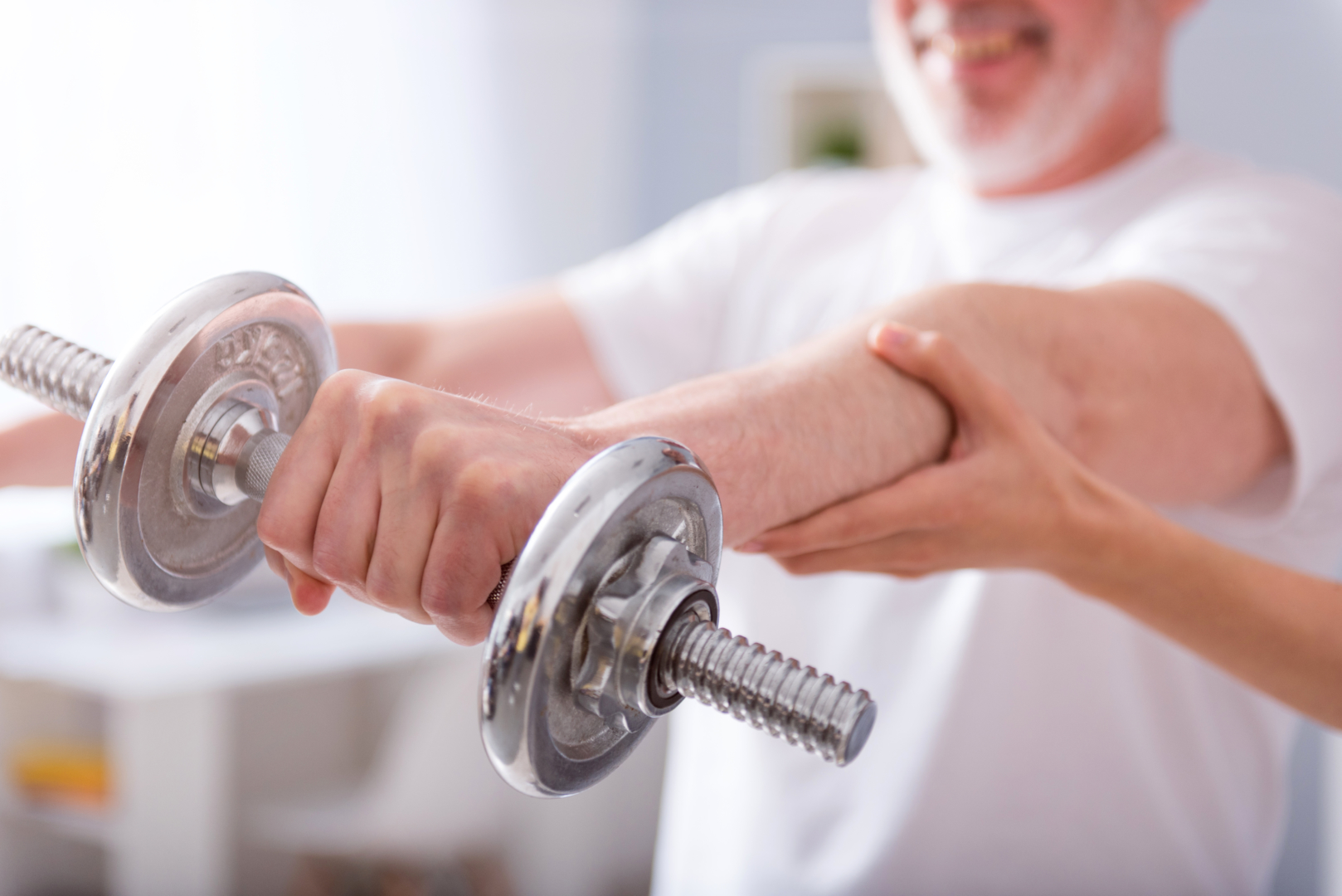 Smiling man using dumbbells to do front lateral raises during physical therapy.